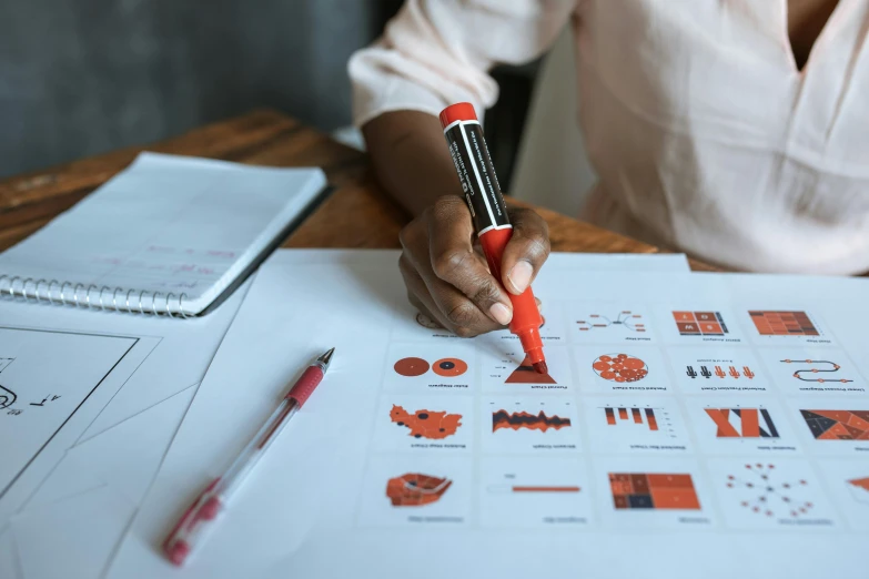 a woman sitting at a table writing on a piece of paper, pexels contest winner, analytical art, informative graphs and diagrams, red and orange color scheme, pointing, school curriculum expert