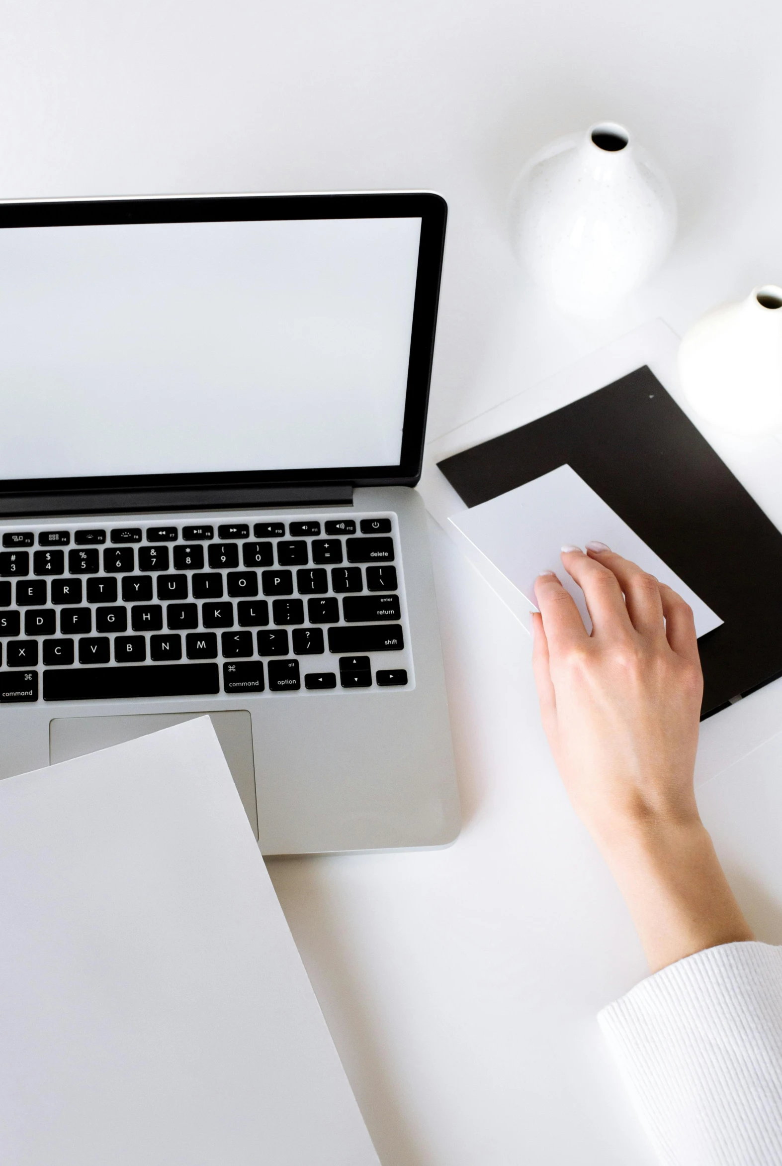 a person sitting at a desk using a laptop computer, white and black color palette, holding it out to the camera, item, without text