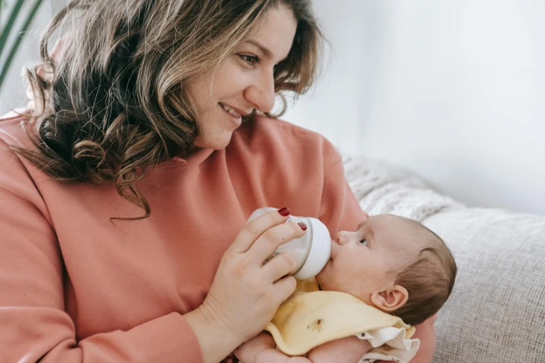 a woman feeding a baby with a bottle, pexels contest winner, white and yellow scheme, brunette, manuka, next to a cup