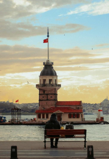 a person sitting on a bench in front of a body of water, by Niyazi Selimoglu, neoclassical tower with dome, harbor, slide show, 256x256