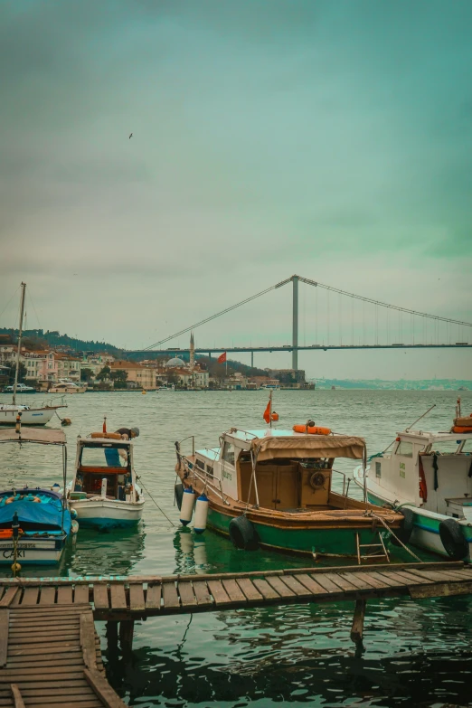 a group of boats sitting on top of a body of water, a colorized photo, by Niyazi Selimoglu, pexels contest winner, hanging bridge!!, square, nice slight overcast weather, today\'s featured photograph 4k