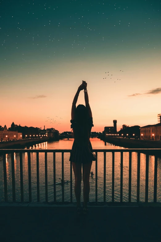 a woman standing on top of a bridge next to a body of water, pexels contest winner, aestheticism, hands in the air, rooftop romantic, early evening, instagram post