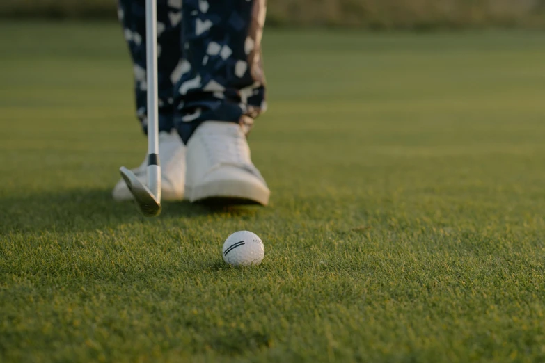 a man standing on top of a green field next to a golf ball, in the evening, upclose, off - putting, leg shot