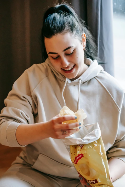 a woman sitting on the floor eating a bag of chips, pexels contest winner, beige hoodie, inside a glass jar, manuka, frosting on head and shoulders