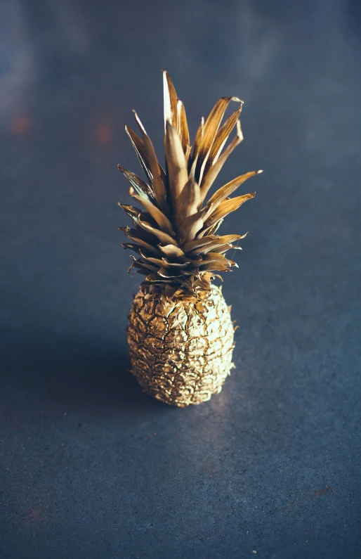 a close up of a pineapple on a table, made of gold, viewed from above, lit from the side, slate