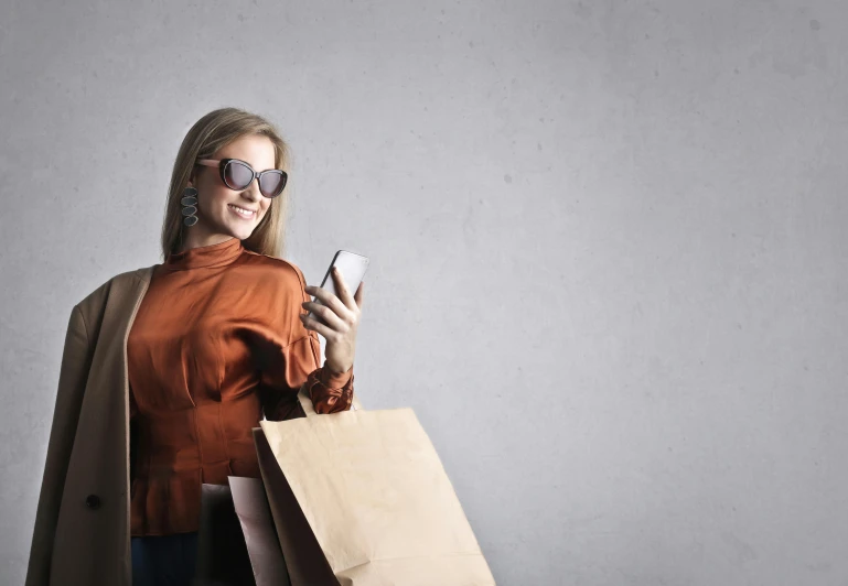 a woman holding shopping bags and a cell phone, a portrait, trending on pexels, renaissance, with sunglass, brown clothes, a large, on grey background