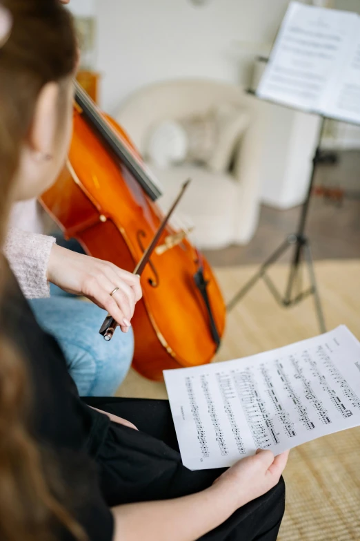 a woman sitting on the floor holding a sheet of music, shutterstock, cello, high quality picture, bassist, sunday afternoon