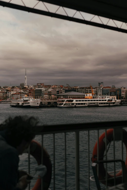 a man sitting at a table in front of a large body of water, istanbul, low quality photo, ships in the harbor, rainy evening