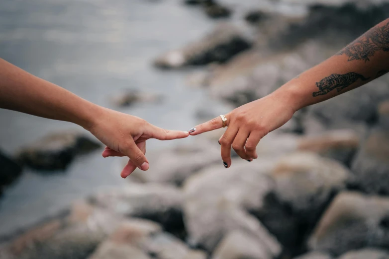 two people holding hands near a body of water, by Lucia Peka, trending on pexels, giving the middle finger, lesbian, chemistry, long distance