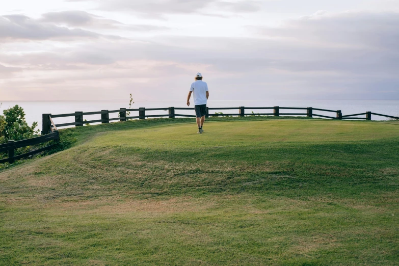 a man standing on top of a lush green hillside, unsplash contest winner, happening, wearing golf shorts, walking away, sydney park, on the coast