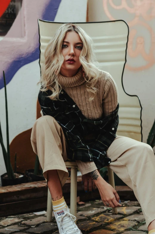 a woman sitting on a chair in front of a painting, a portrait, inspired by Elsa Bleda, trending on pexels, graffiti, sydney sweeney, brown sweater, grunge style, promotional image