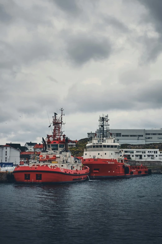 a couple of boats that are in the water, by Roar Kjernstad, pexels contest winner, modernism, industrial colours, grey skies, rugged ship captain, red magic surrounds her