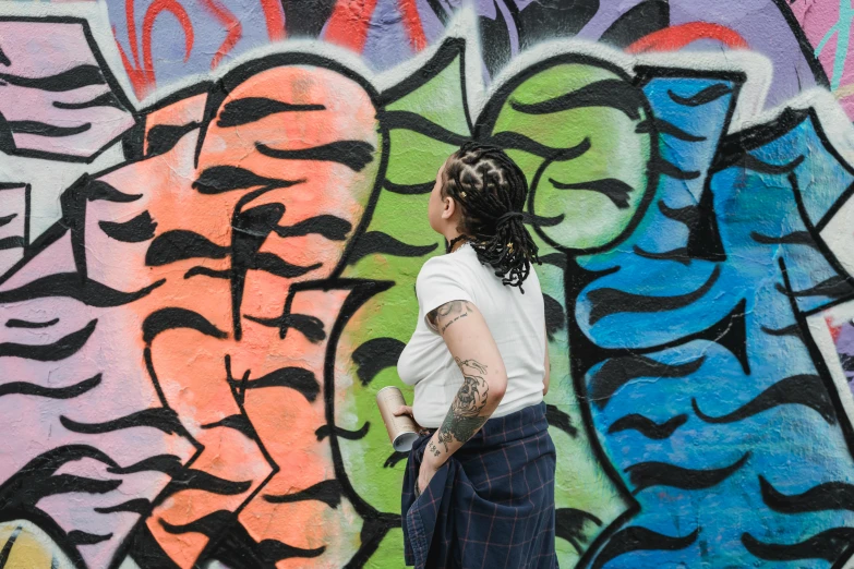 a woman standing in front of a graffiti covered wall, a photo, dreadlock hair, standing with her back to us, lgbtq, background image
