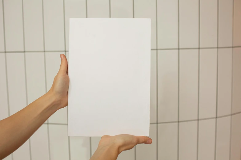 a person holding a piece of paper in their hand, inspired by Agnes Martin, unsplash, private press, made of all white ceramic tiles, in a bathroom, large vertical blank spaces, product introduction photo