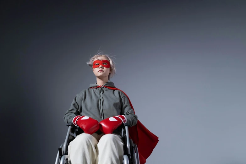 a woman in a wheelchair with a red cape, inspired by Harriet Powers, trending on pexels, grey, super hero pose, utilitarian, press shot