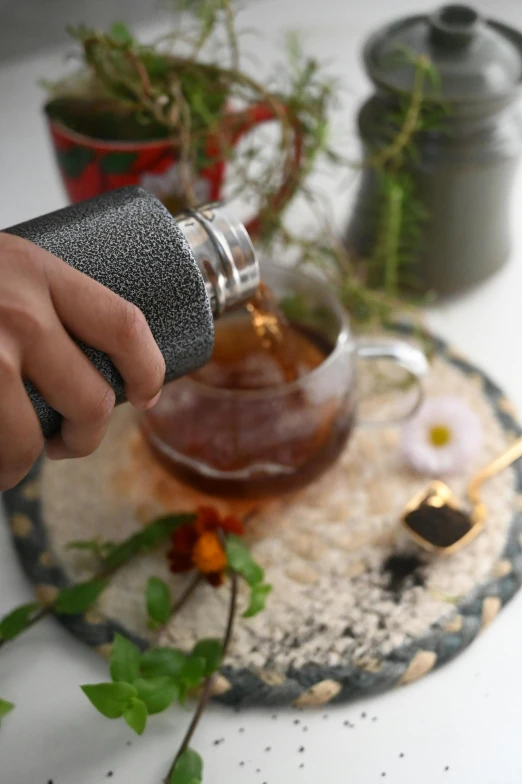 a person pouring tea into a cup on a table, a stipple, inspired by Kanō Tan'yū, unsplash, flasks in hands, hero shot, neoprene, intricately detailed textures