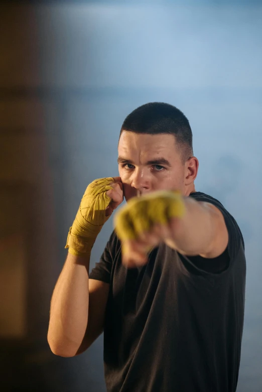 a man in a black shirt and yellow boxing gloves, inspired by Carlos Berlanga, pointing, promo image, profile image, aged 2 5