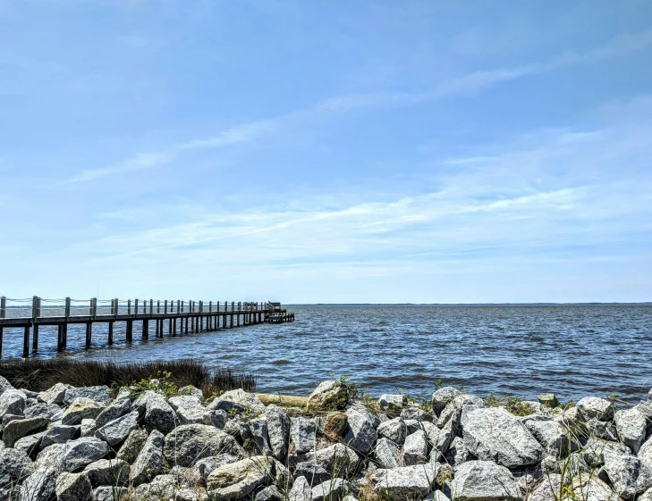 a pier in the middle of a large body of water, by Carey Morris, pexels, rocky lake shore, views to the ocean, brown, may)