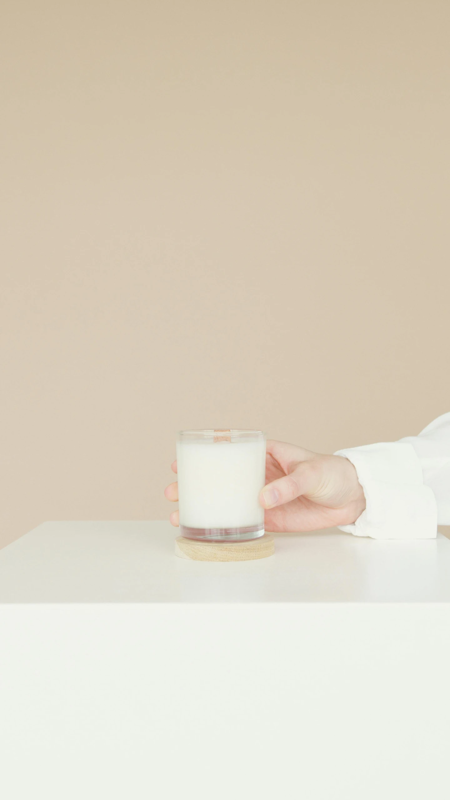 a woman sitting at a table with a glass of milk, minimalism, candle wax, modern minimal design, hand, white