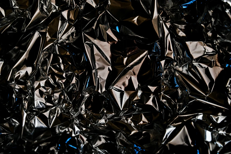 a pile of tin foil sitting on top of a table, an abstract sculpture, by Julia Pishtar, pexels contest winner, plasticien, solid black #000000 background, blue-black, panel of black, mars black