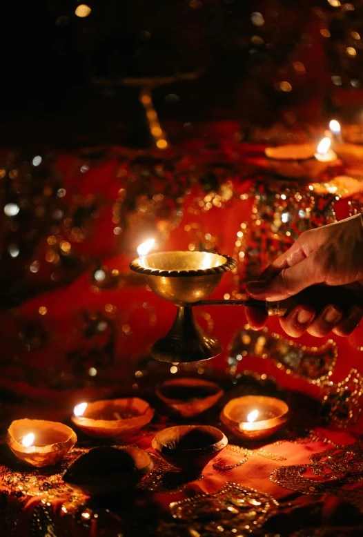 a woman is lighting candles on a table, trending on pexels, visual art, hindu ornaments, golden embers flying, more intense, 2010s