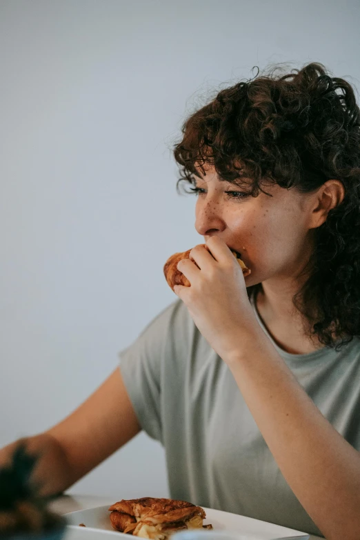 a woman sitting at a table with a plate of food, eating garlic bread, profile image, mullet, slightly minimal