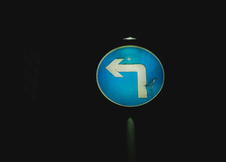 a close up of a street sign on a pole, by Matija Jama, unsplash, symbolism, out in the dark, arrow shaped, round, blue