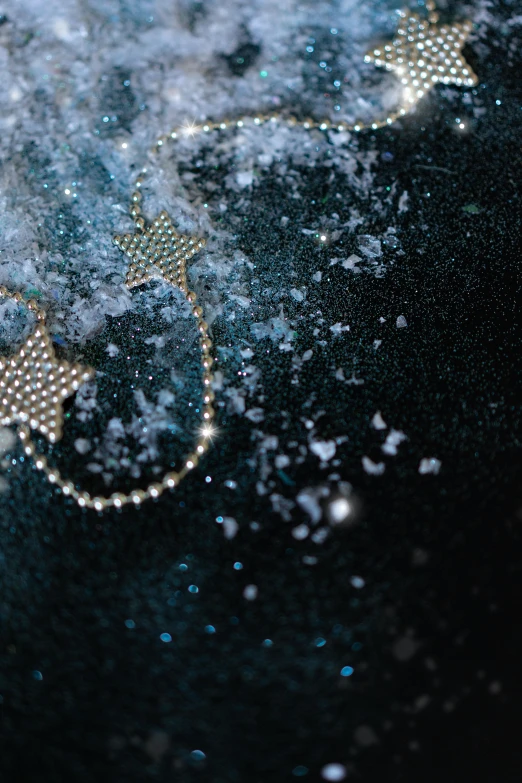 a pair of scissors sitting on top of a table covered in snow, glittering stars scattered about, blue jewellery, black background with stars, splash image