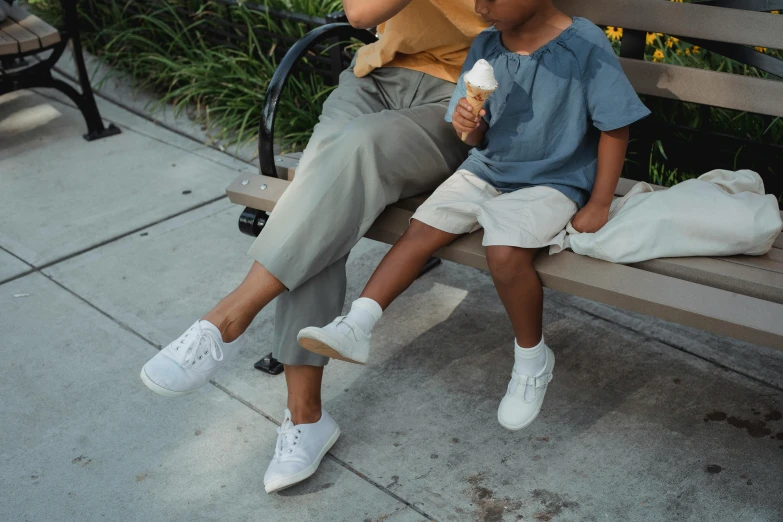 a woman sitting next to a child on a bench, trending on pexels, wearing white sneakers, khakis, promotional image, ice cream