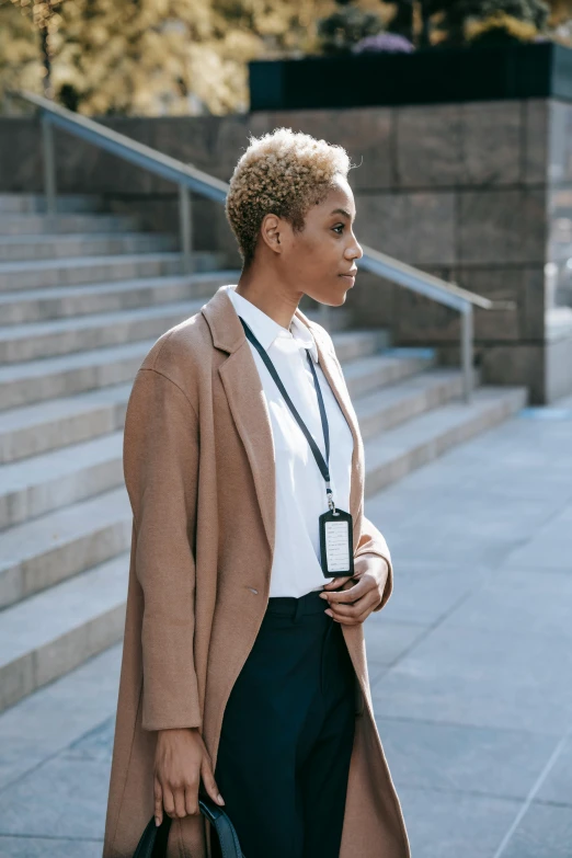 a woman walking down a sidewalk with a handbag, trending on pexels, renaissance, short blonde afro, serious business, wearing jacket, she is holding a smartphone