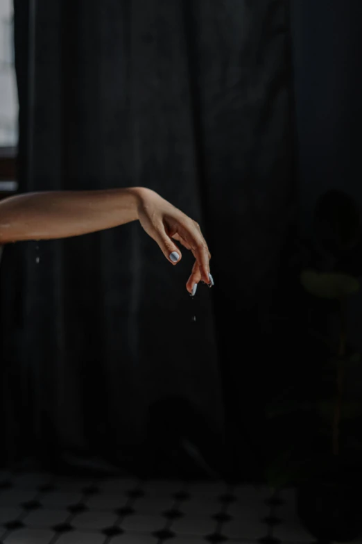 a woman standing in front of a window holding a cigarette, by Elizabeth Polunin, unsplash, realism, two hands reaching for a fish, on black paper, modern dance aesthetic, prosthetic arm