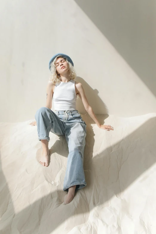 a woman laying on top of a bed in a white room, inspired by Elsa Bleda, trending on pexels, baggy jeans, baggy clothing and hat, pale blue outfit, sun flairs