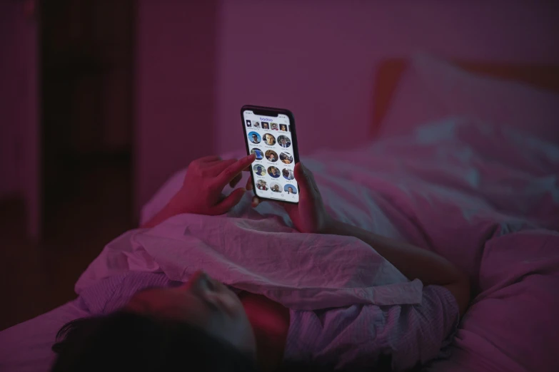 a person laying in bed with a cell phone, a picture, pink lighting, dark screen, multiple stories, gen z