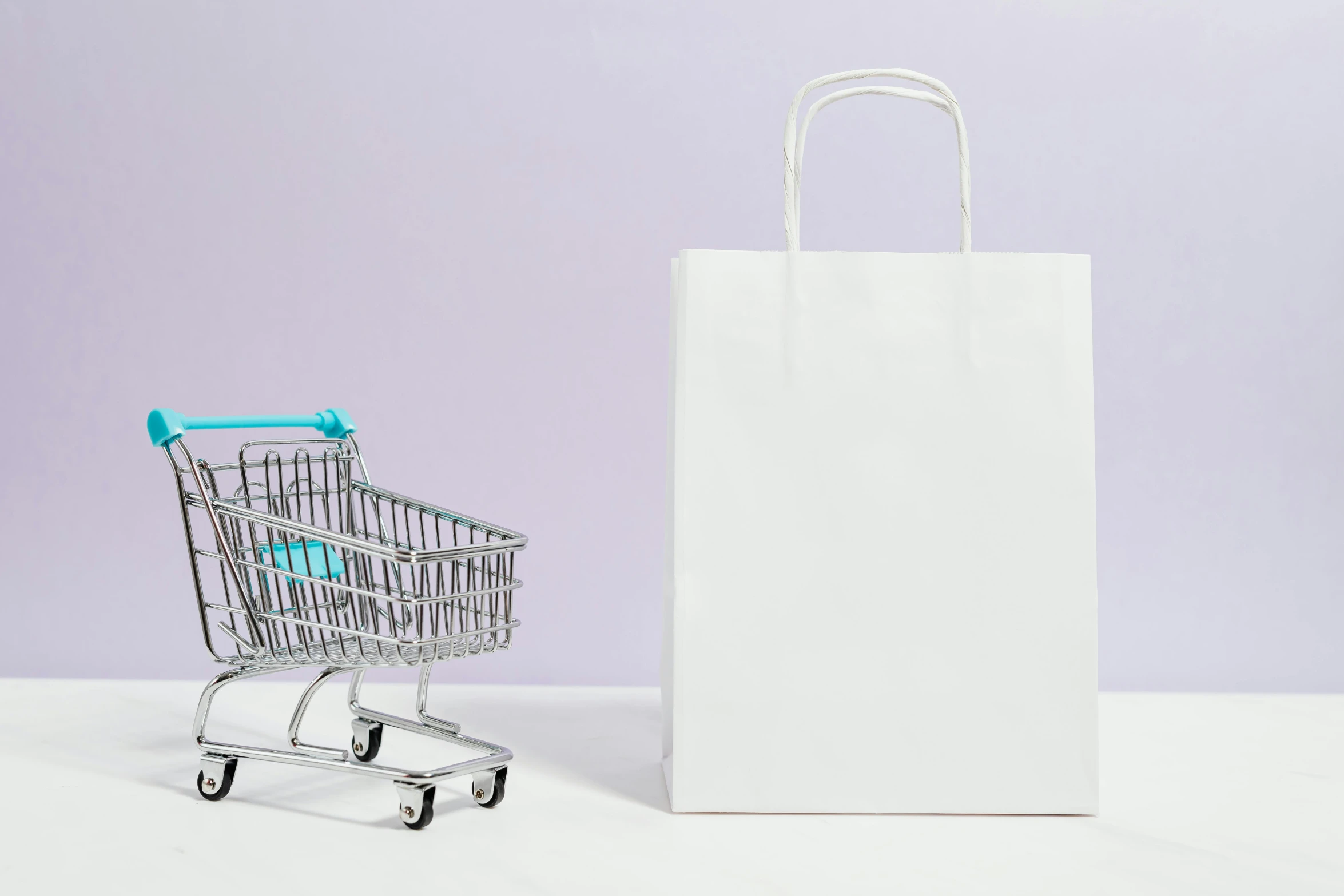 a shopping cart sitting next to a shopping bag, by Julia Pishtar, trending on unsplash, postminimalism, emma bridgewater and paperchase, background is white and blank, purple blue color scheme, white table