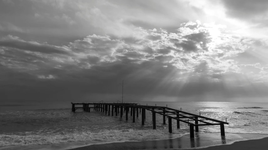 a black and white photo of a pier in the ocean, by Colijn de Coter, pexels contest winner, romanticism, sunrays between clouds, :: morning, after the storm, sun coast