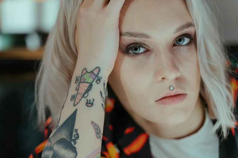 a woman with a tattoo on her arm, inspired by Elsa Bleda, trending on pexels, hyperrealism, androgynous face, septum piercing, young blonde woman, frightened look