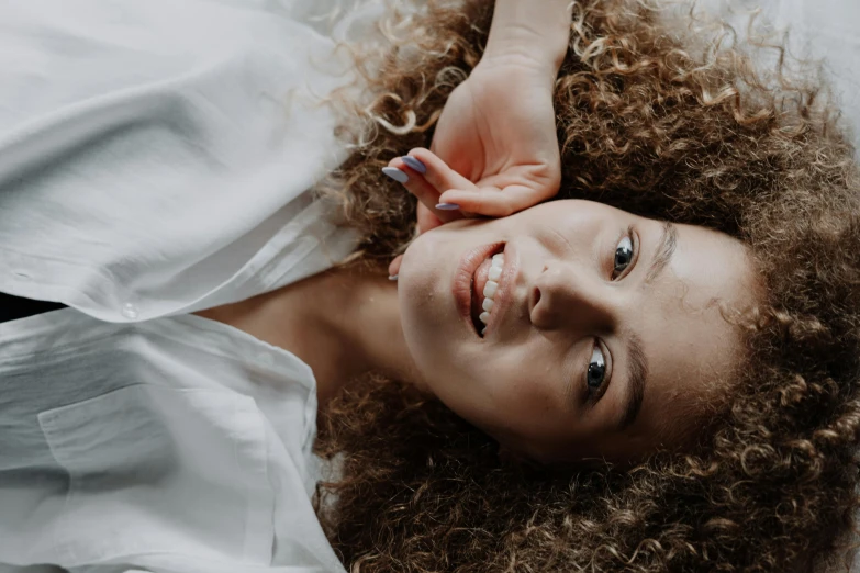 a beautiful young woman laying on top of a bed, trending on pexels, renaissance, curly middle part haircut, white teeth, zoomed in, ilustration