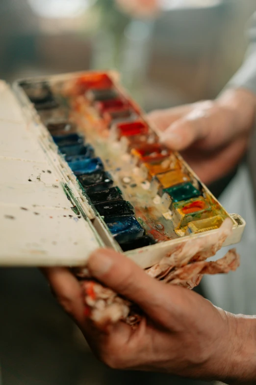 a close up of a person holding a box of paint, a watercolor painting, trending on pexels, visual art, rich decaying bleeding colors, burnt umber and blue, petite, palettes