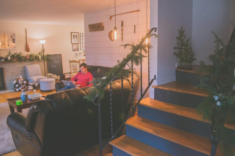 a man sitting on a couch in a living room, long winding stairs going down, holiday vibe, black fir, working hard