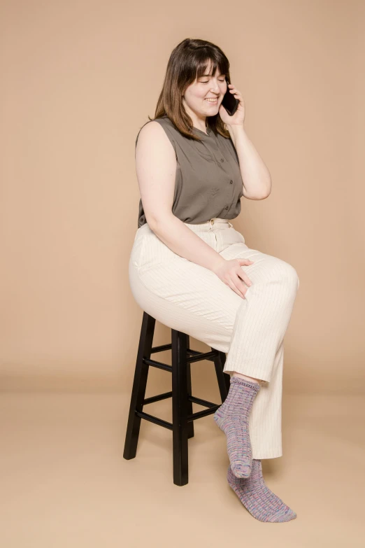 a woman sitting on a stool talking on a cell phone, non binary model, white pants, high soles, lilac