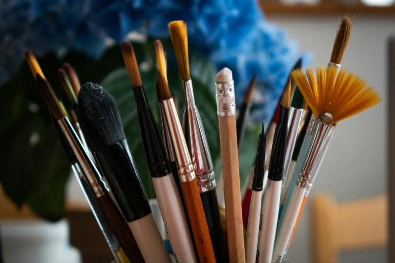 a vase filled with lots of brushes sitting on top of a table, a photorealistic painting, trending on pexels, medium close up shot, holding paintbrushes, 🎨🖌, feat of artistic achievement