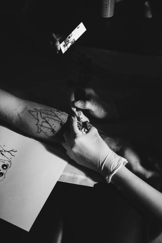 a person holding a piece of paper with a drawing on it, a tattoo, by Adam Marczyński, pexels contest winner, black and white paint, surgeon, evening time, dotting