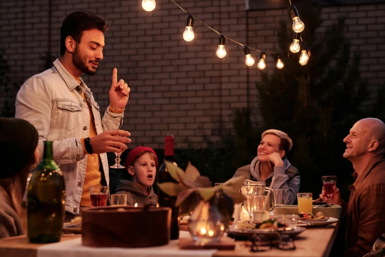 a group of people sitting around a dinner table, outdoor lighting, giving the middle finger, holiday season, hipster dad