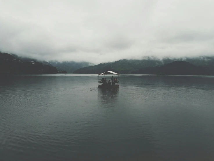 a boat floating on top of a lake under a cloudy sky, sumatraism, dark grey, lake house, foggy rainy day, lo-fi