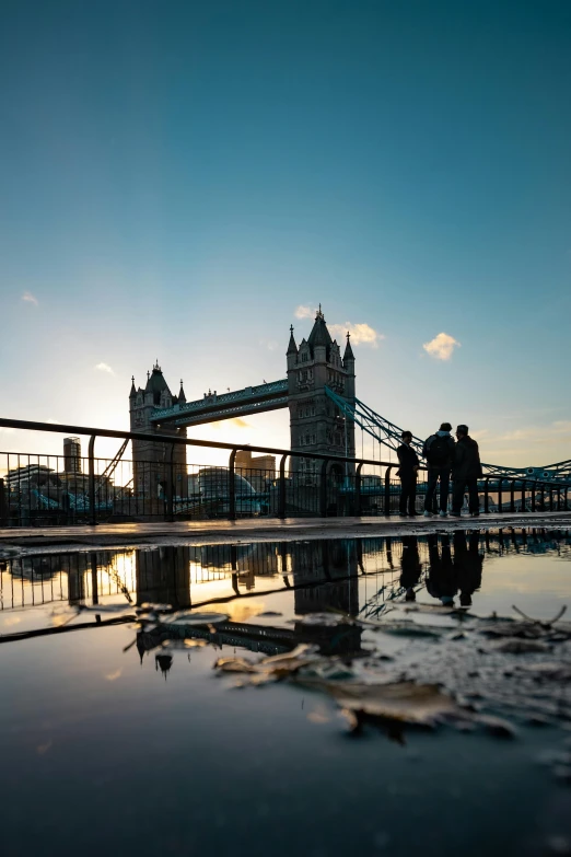 a group of people standing on top of a bridge, tower bridge, at the golden hour, flooding, splash image