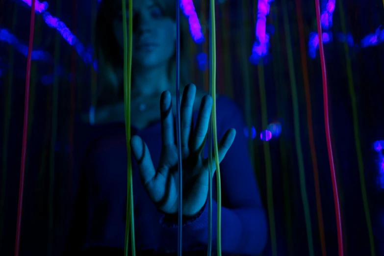 a woman standing in front of a bunch of strings, a hologram, pexels, interactive art, hand controlling, taken in night club, suspiria, purple and blue neon