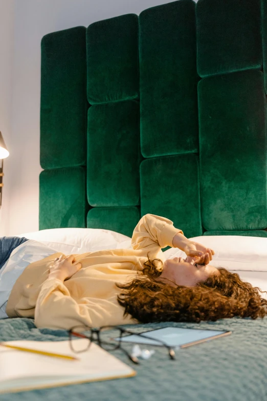 a woman laying on a bed with a green headboard, inspired by Elsa Bleda, trending on pexels, renaissance, hotel room, curls, rectangle, uplit