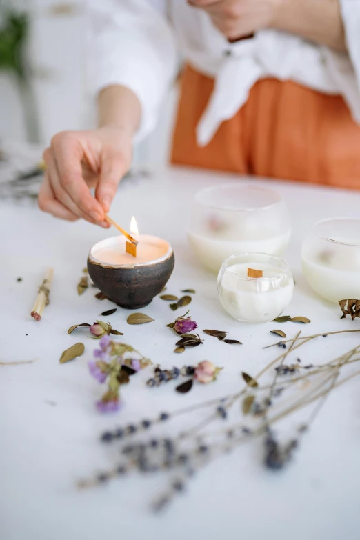 a woman lighting a candle on a table, a still life, trending on unsplash, natural materials, multi-part, on white background, made of glazed