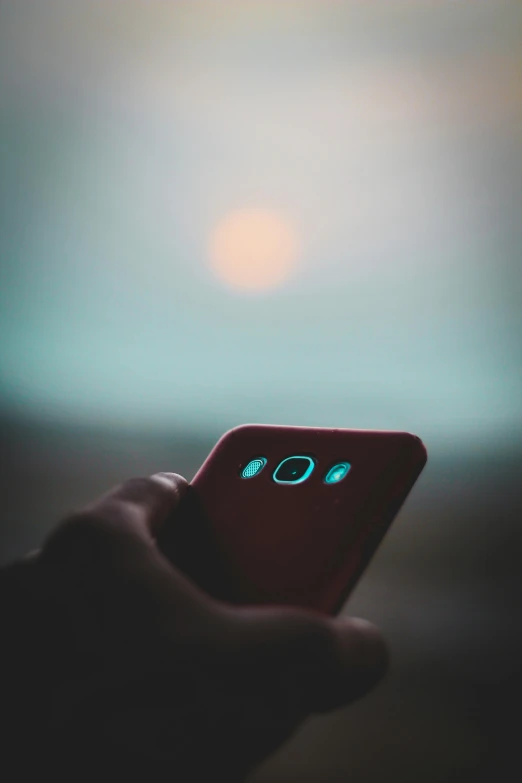 a person holding a cell phone in their hand, a picture, by Ryan Pancoast, trending on pexels, minimalism, glowing buttons, android close to camera, the sky is a faint misty red hue, teal lights