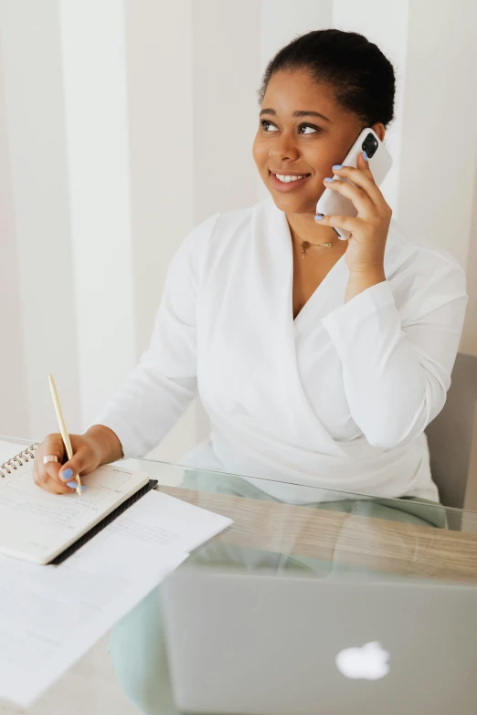 a woman sitting at a desk talking on a cell phone, wearing white v - neck top, holding notebook, curated collections, essence